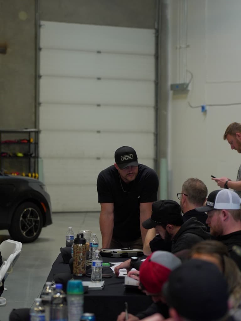 A workshop speaker presenting to wrap shop owners taking notes around tables in the warehouse classroom