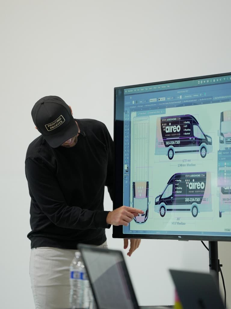 Workshop facilitator pointing at an Illustrator file showing real commercial van wrap mockups for the AireoHome service brand
